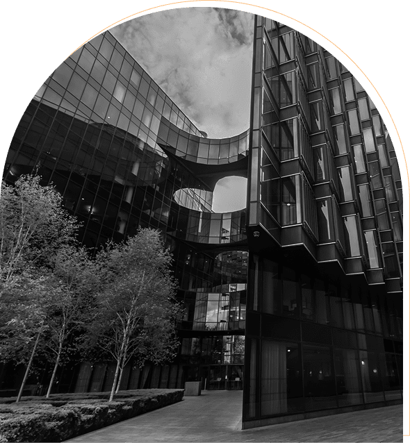 Modern glass buildings with a sky bridge and trees below.